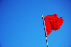 Red Colored Flag Fluttering in the Wind Against a Blue Sky
