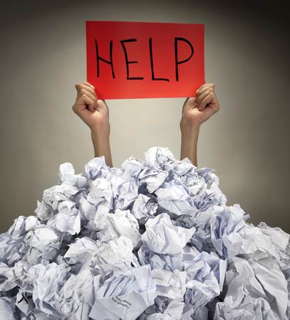 College Graduate Holding Up a 'HELP' Sign from Under a Heap of Crumpled Papers